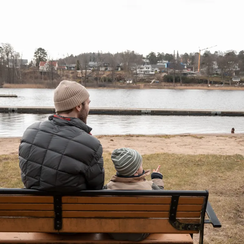 A father and his child on a bench by a lake, seen from behind